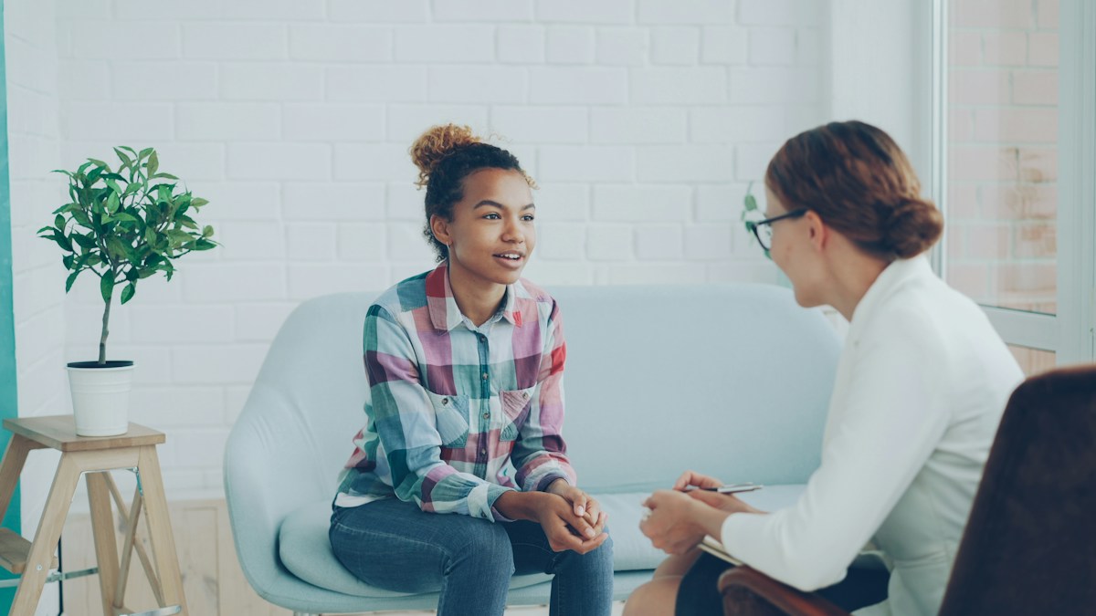 An adult woman talking with a therapist who listens and takes notes in a naturally lit office